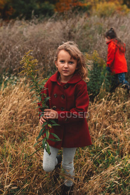 Retrato de niña y su hermana recogiendo flores silvestres en el campo - foto de stock