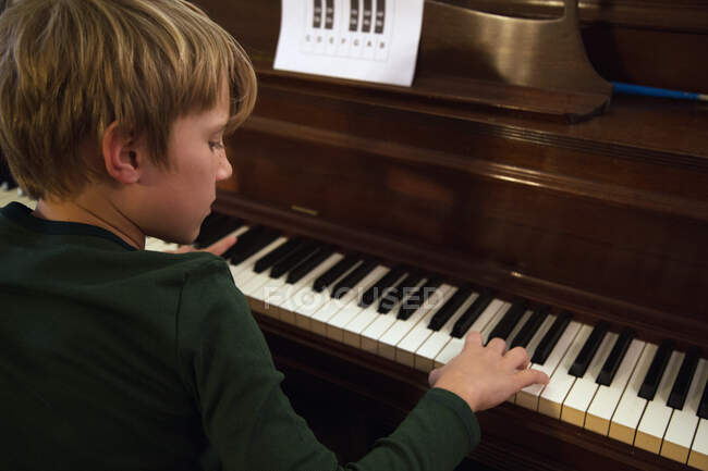 Vista sobre el hombro del niño tocando el piano en la sala de estar - foto de stock