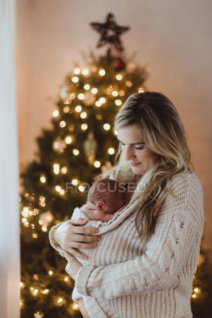 Mulher adulta berço bebê recém-nascido filha envolto em casaco de lã no Natal — Fotografia de Stock