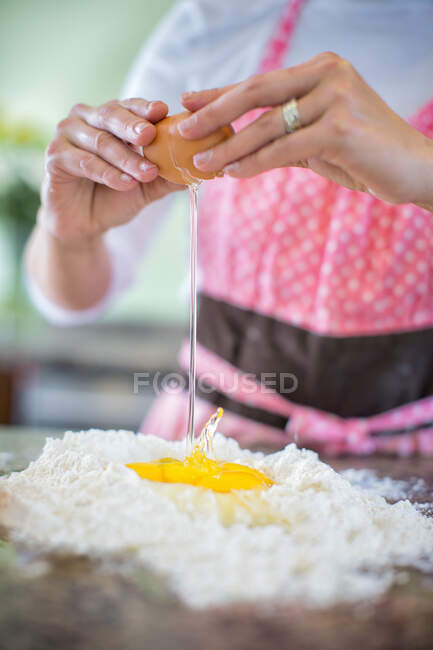 Зрелая женщина разбивает яйцо на муку, посередине — стоковое фото