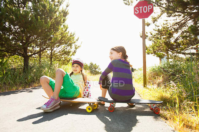 Girls sitting on skateboards along rural road — Stock Photo