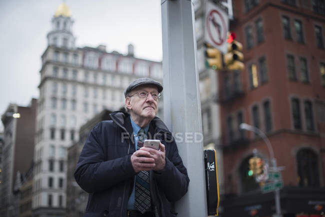Mann lehnt an Laternenpfahl, hält Smartphone, Manhattan, New York, USA — Stockfoto