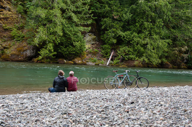 Vista trasera de la pareja en la orilla del río mirando hacia otro lado, Packwood, Washington, EE.UU. - foto de stock