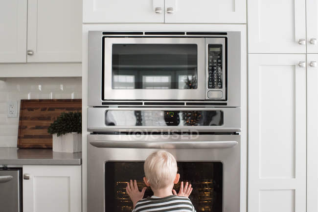 Boy in kitchen looking through oven door — Stock Photo