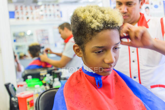 Hairdresser cutting teenage boy's hair in barbershop — Stock Photo