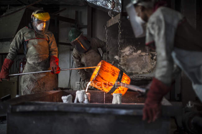 Metalworkers working in foundry, pouring molten bronze — Stock Photo