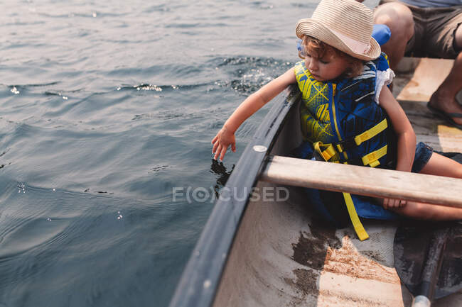 Девушка касается воды с гребной лодки на озере — стоковое фото