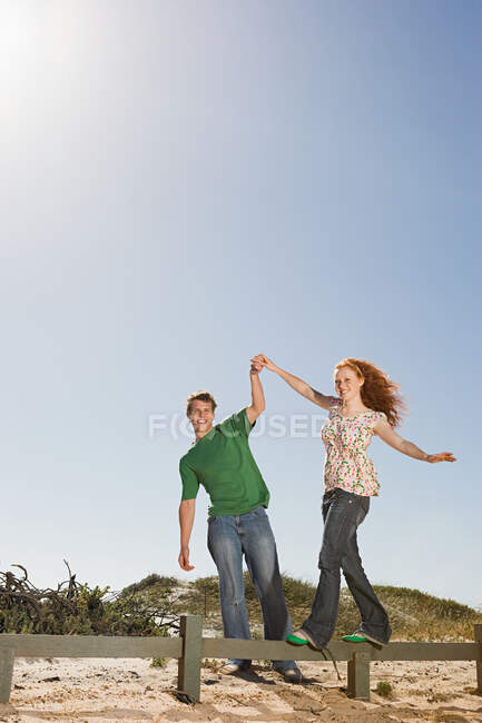 Молодой человек помогает женщине балансировать на заборе — стоковое фото