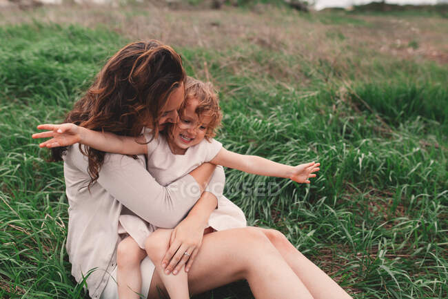 Девушка сидит на коленях у матери на ветреном поле — стоковое фото