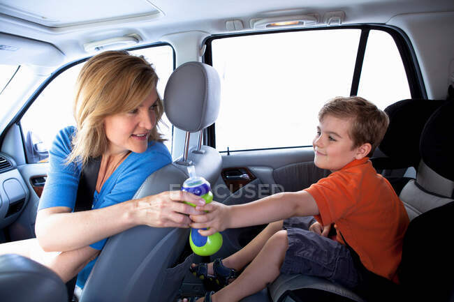 Madre pasando botella a niño en el asiento trasero del coche - foto de stock