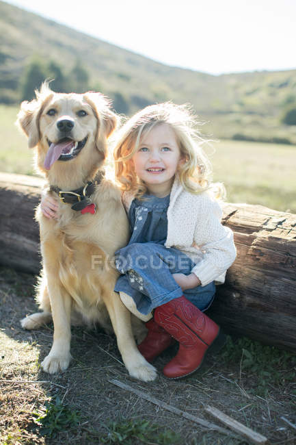 Portrait of girl and dog sitting by log — Stock Photo