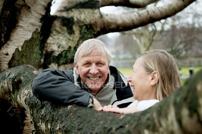 Старша пара, спираючись на дерево, посміхається — стокове фото