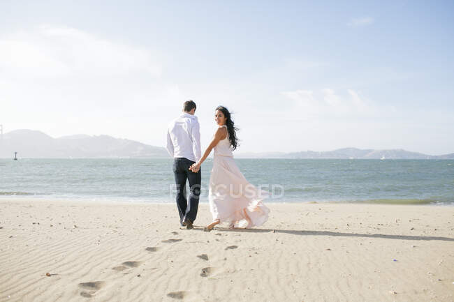 Frau blickt zurück, während sie Hand in Hand mit Freund am Strand spaziert — Stockfoto
