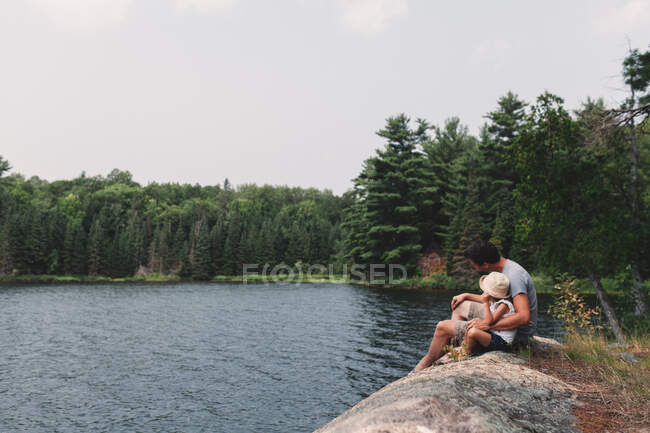 Jovem e filha sentados na rocha à beira de um lago — Fotografia de Stock