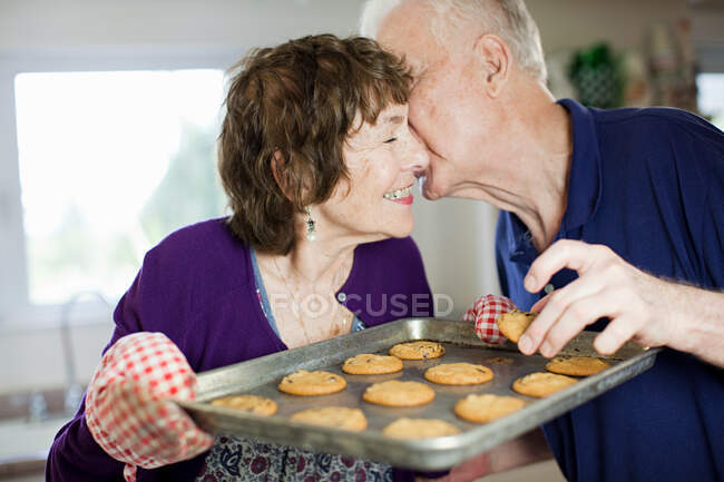 Seniorenpaar küsst sich mit selbst gebackenen Plätzchen — Stockfoto