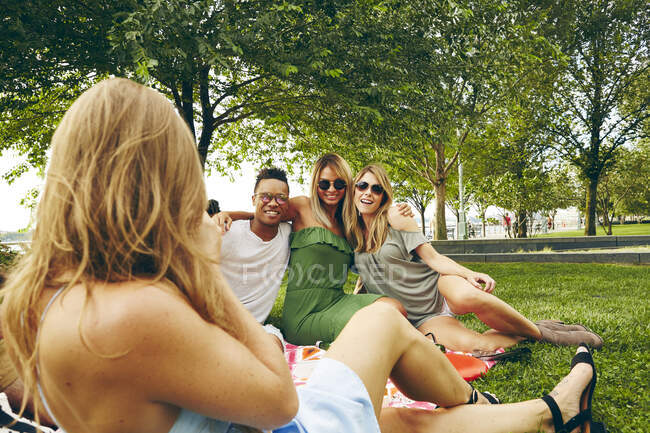 Vista sobre el hombro de la mujer fotografiando a amigos haciendo picnic en el parque - foto de stock