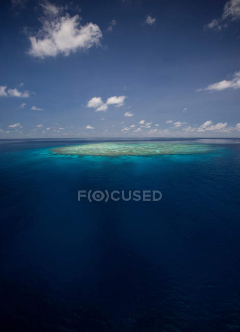 Безлюдний острів у блакитному морі проти неба з хмарами — стокове фото