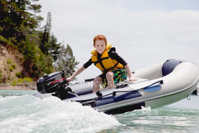 Мальчик, управляющий моторной шлюпкой в море — стоковое фото