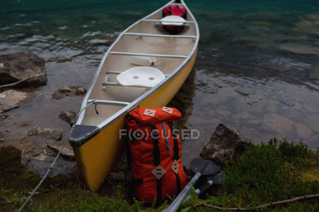 Orange color backpack leaning against yellow canoe — Stock Photo
