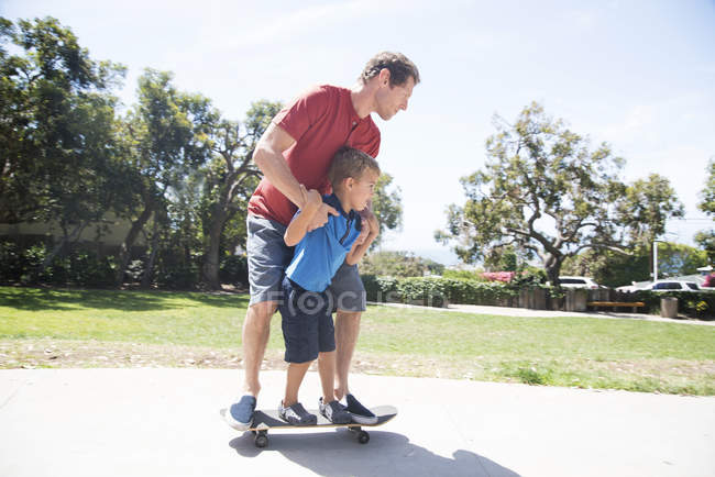 Отец и сын в парке практикуют скейтбординг — стоковое фото