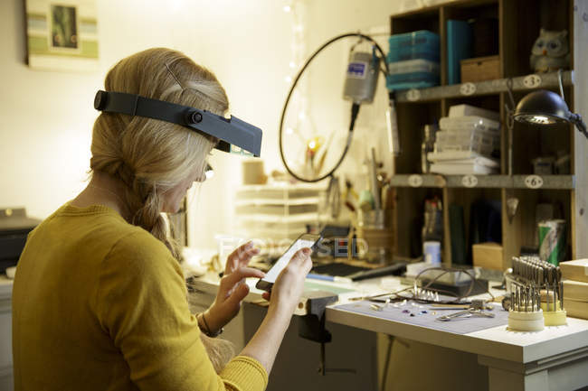 Créatrice de bijoux utilisant un écran tactile pour smartphone dans un studio de design — Photo de stock