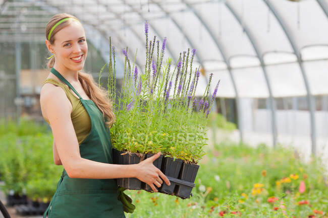 Mid adult woman holding plants in garden centre, portrait — Stock Photo