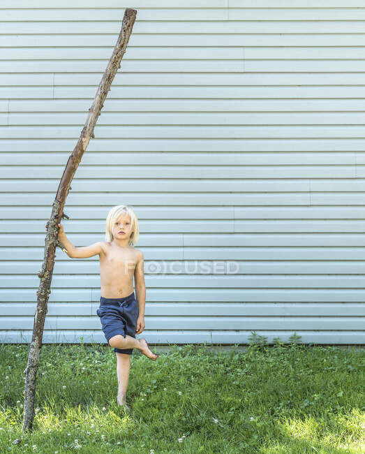 Junge steht auf einem Bein und hält Stock — Stockfoto