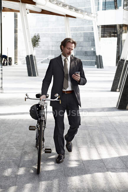 Homem de negócios adulto médio andando com bicicleta e usando telefone celular — Fotografia de Stock