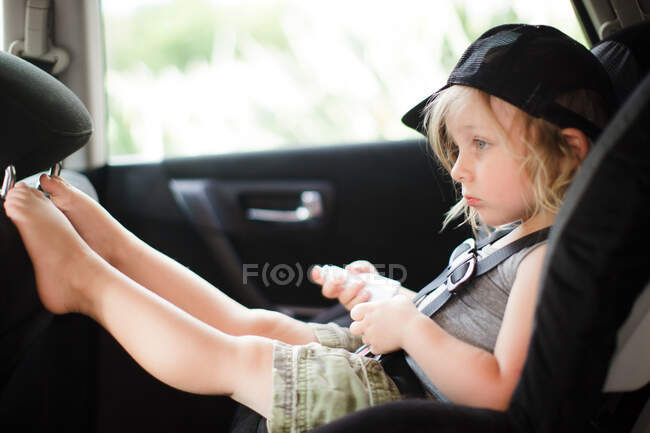 Enfant mâle avec les pieds vers le haut regardant dans le siège arrière de la voiture — Photo de stock