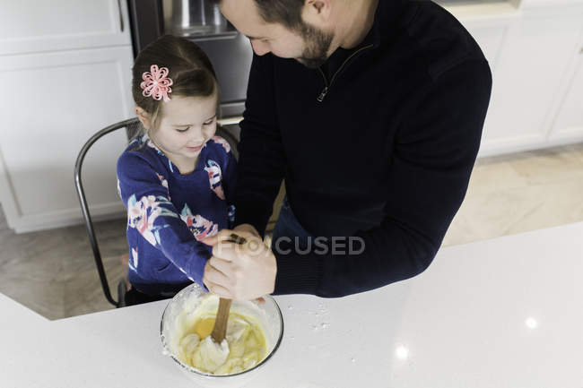 Mid adult man and daughter stirring mixing bowl together at kitchen counter — Stock Photo