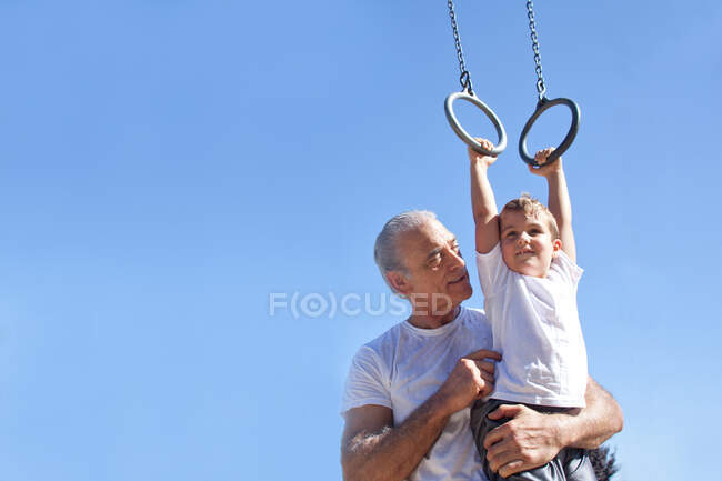 Grandfather holding grandson on gymnastic rings — Stock Photo