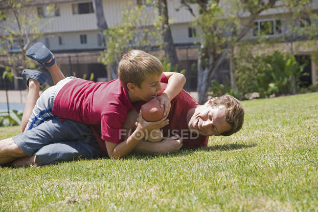 Син розмовляє батьком, граючи в американський футбол у парку — стокове фото