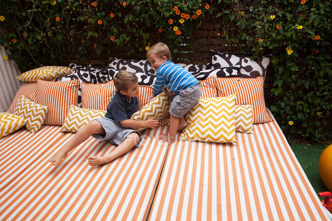 Dois meninos brincando em móveis ao ar livre com almofadas — Fotografia de Stock