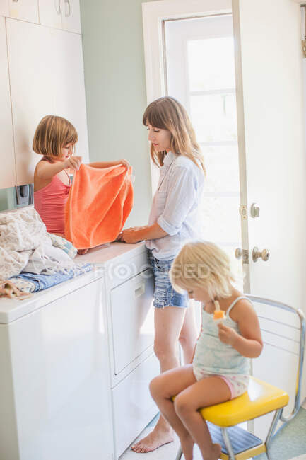 Madre con due figlie pieghevole lavanderia in ripostiglio — Foto stock