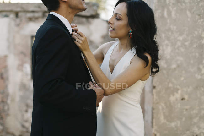 Noiva e noivo ao ar livre, noiva endireitando noivo gravata pescoço — Fotografia de Stock