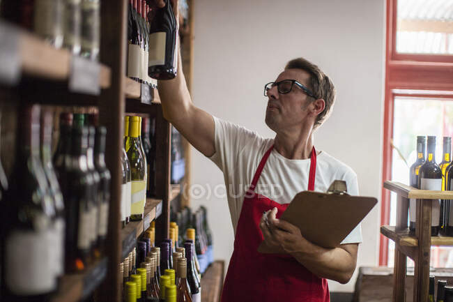 Cape Town, South Africa, young male wine shopkeeper raising a bottle of wine with notepad in his hand — Stock Photo