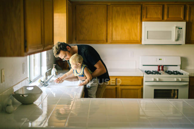 Padre e hijo pequeño lavándose las manos en el fregadero - foto de stock