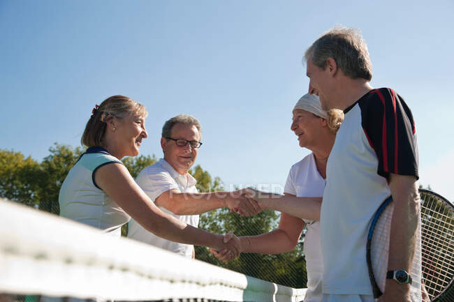 Senior and mature adults shaking hands on tennis court — Stock Photo