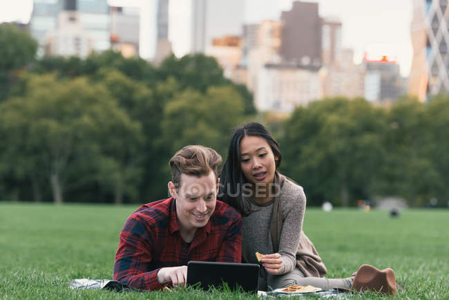 Mediados de pareja adulta en manta de picnic lectura tableta digital en Central Park, Nueva York, Estados Unidos - foto de stock