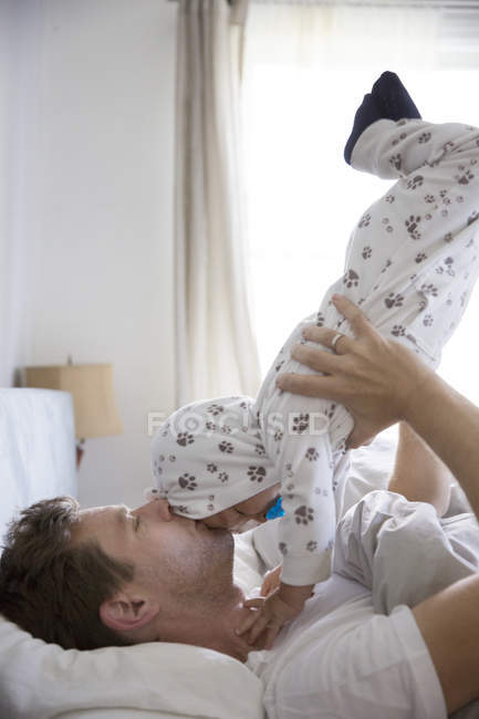 Pai deitado na cama, levantando o jovem filho no ar — Fotografia de Stock