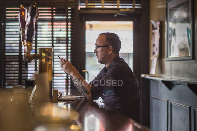 Barman reading smartphone texts at public house counter — Stock Photo