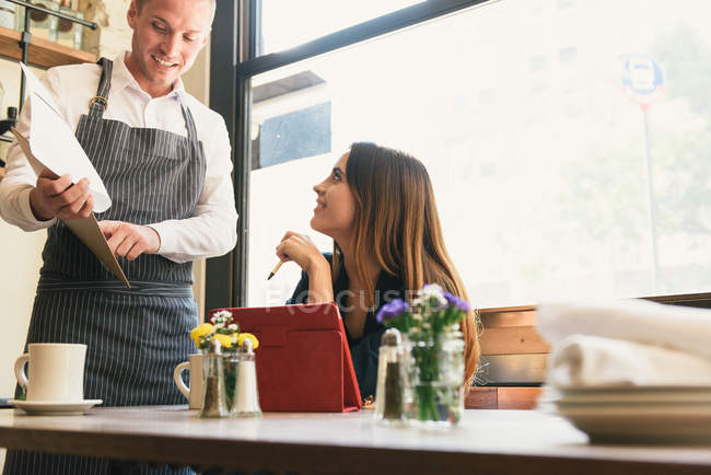 Giovane donna e cameriere discutendo menu nel ristorante — Foto stock