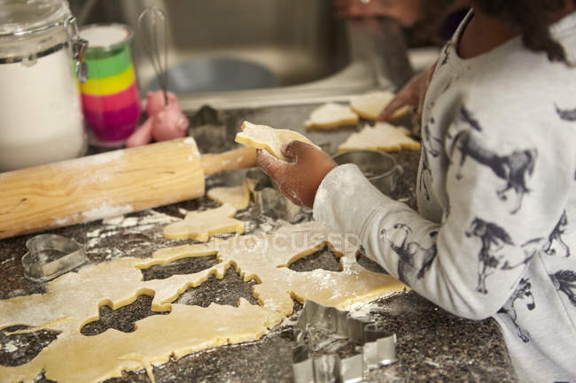Chica corte masa de galletas con cortadores de galletas - foto de stock