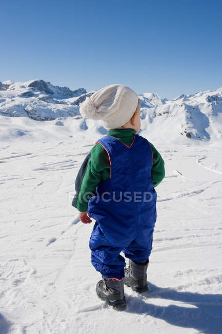 Молодий хлопчик стоїть, дивлячись на гори в снігу — стокове фото
