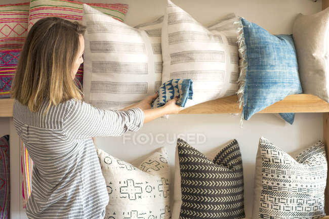Vista trasera de la diseñadora de interiores femenina probando textil contra cojines en estudio minorista - foto de stock