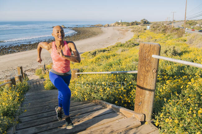 Молодая женщина занимается спортом, бегает вверх по ступенькам возле пляжа, возвышенный вид — стоковое фото
