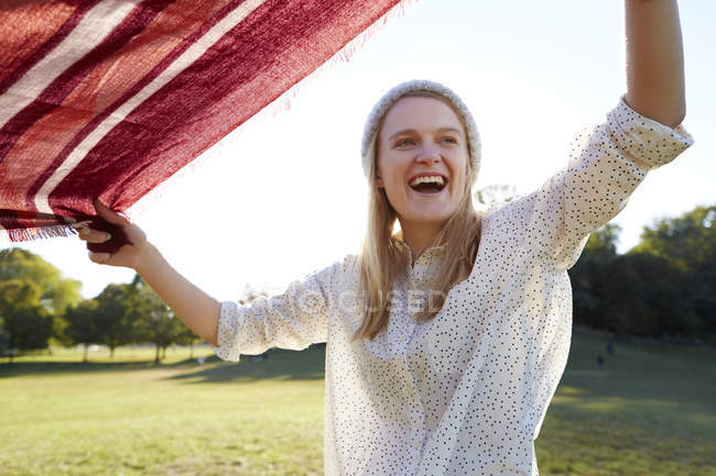 Mujer joven sacudiendo manta de picnic en el parque - foto de stock