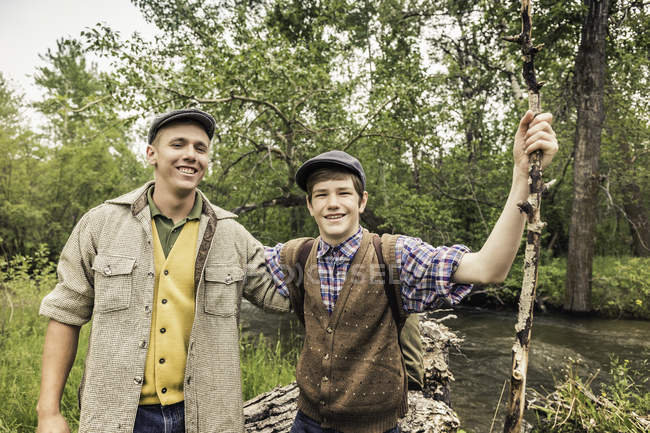 Hombre y niño llevando gorras planas junto al río, mirando a la cámara sonriendo - foto de stock
