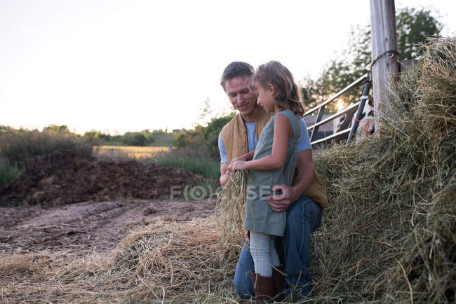 Отец и дочь стоят вместе на ферме, дочь держит сено — стоковое фото