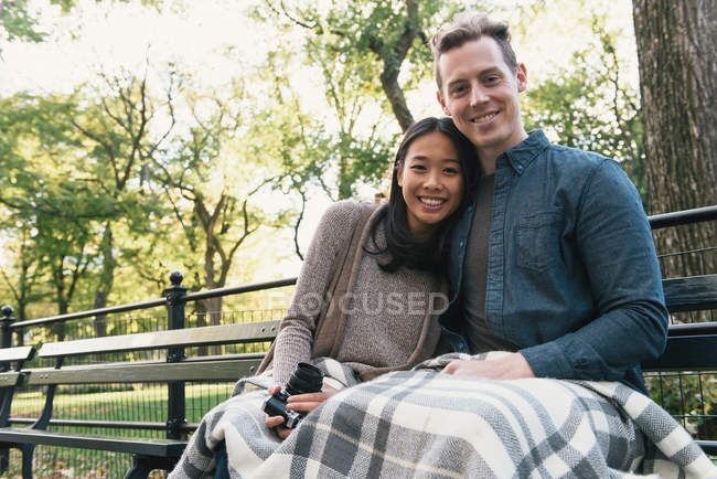 Retrato de pareja adulta sentada en el banco del parque sosteniendo la cámara SLR - foto de stock